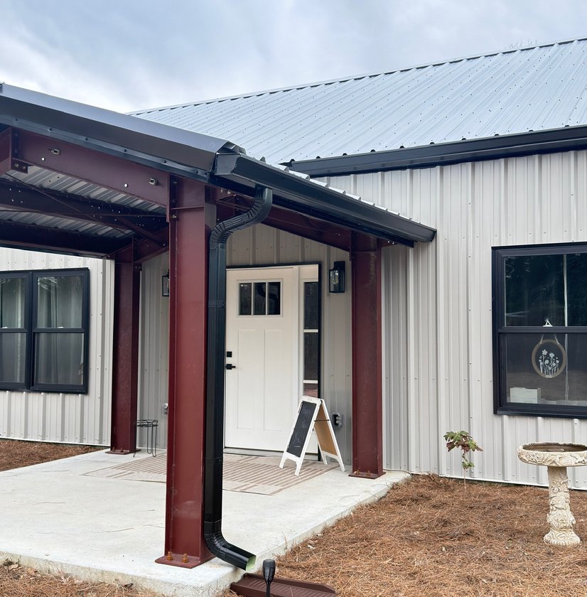 Black gutter and downspout installed on a metal-roofed porch