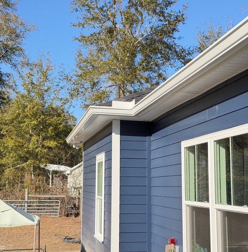 New white seamless gutter along the roofline of a blue-sided home