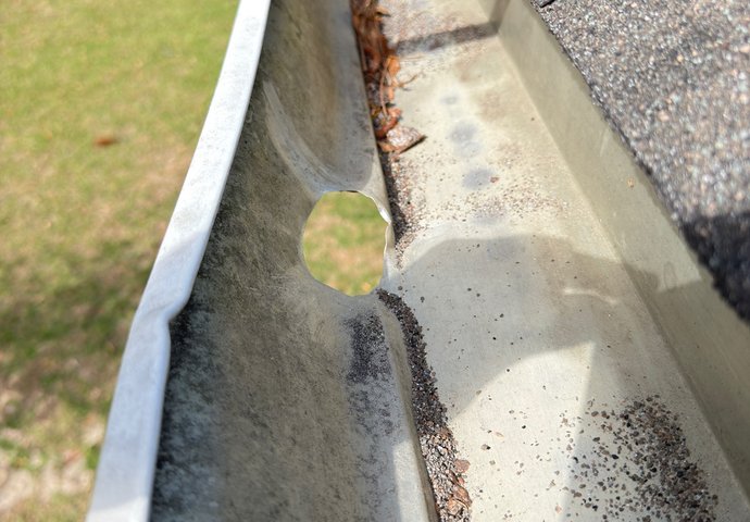 Damaged gutter with a hole and built-up debris in need of repair